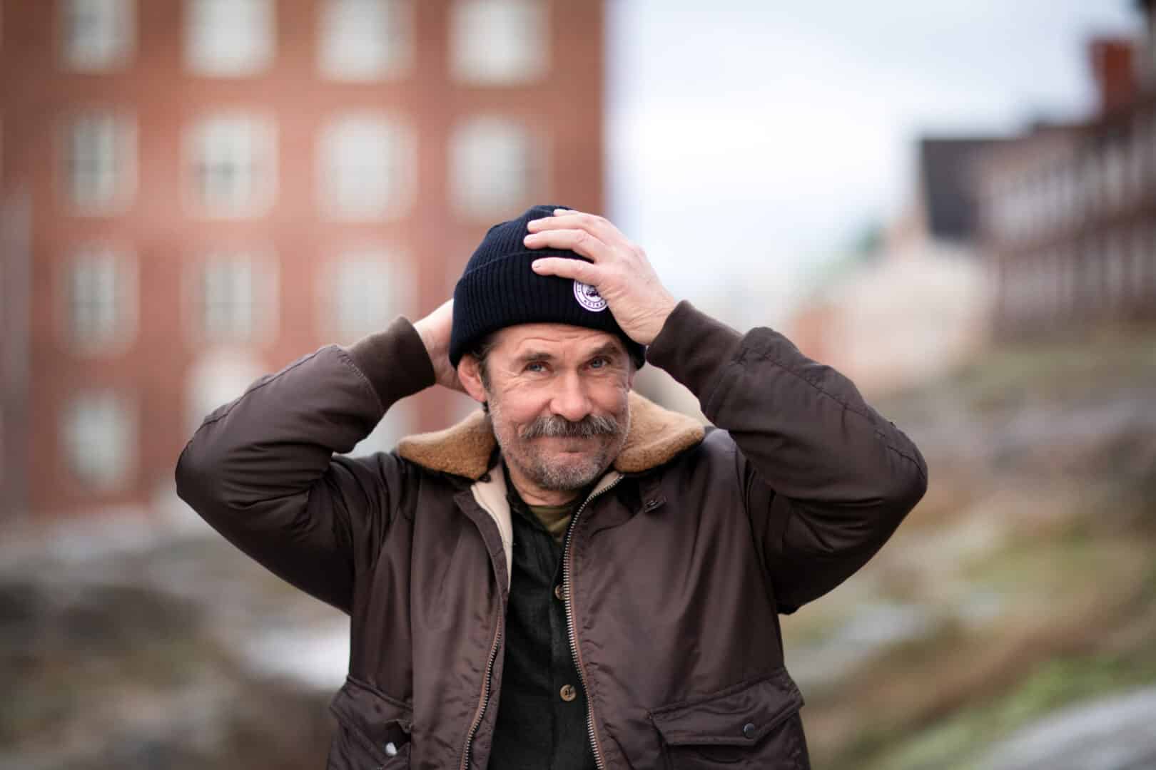 Tommi korpela korjailee mustan piponsa asentoa. Taustalla punatiilinen kerrsptalo helsingin Töölössä.