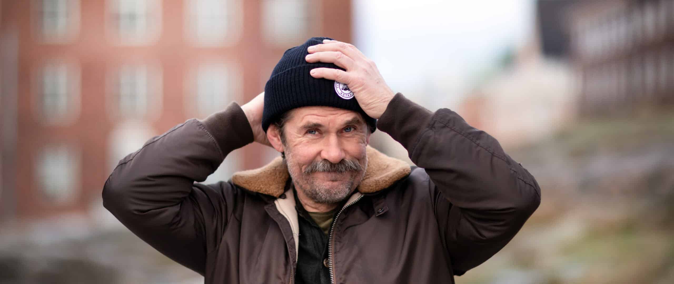 Tommi korpela korjailee mustan piponsa asentoa. Taustalla punatiilinen kerrsptalo helsingin Töölössä.